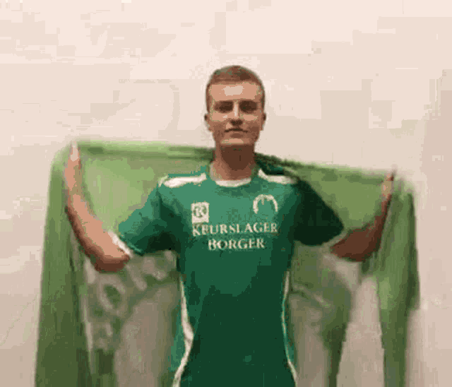 a man wearing a green shirt is holding a green scarf around his neck .
