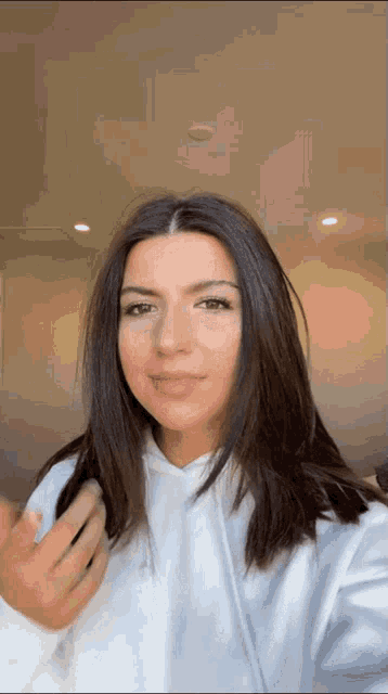 a woman in a white hoodie is taking a selfie with her hand in her hair .