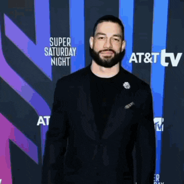 roman reigns is standing on a red carpet in front of a blue and purple background .