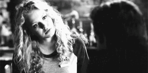 a black and white photo of a woman with curly hair looking at a man in a bar .