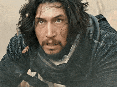 a man with long hair and a beard is wearing a black jacket and a scarf around his neck .
