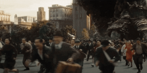a crowd of people running down a street with a monster in the background