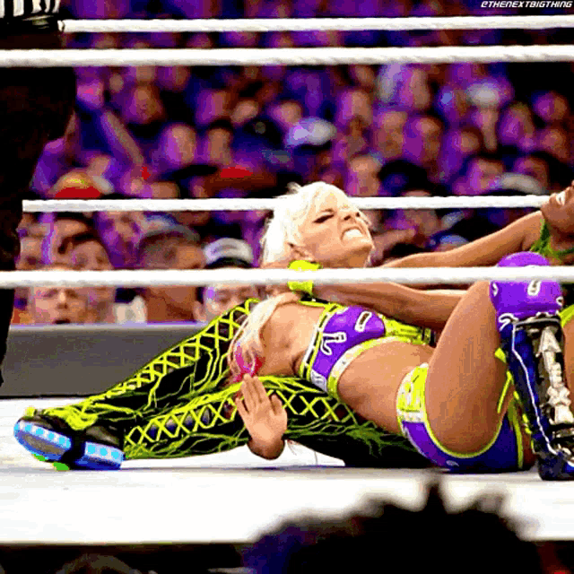 a female wrestler is laying on the ground in a wrestling ring while a referee looks on .