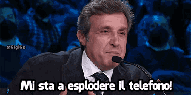 a man in a suit and tie speaking into a microphone with the words " mi sta a esplodere il telefono " above him