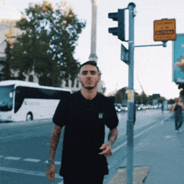 a man wearing a black shirt with the letter h on the front walks down a street