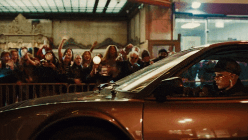 a man is driving a car with a crowd behind him