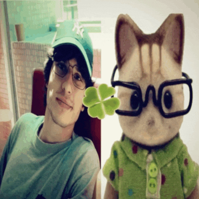 a man wearing glasses holds a green clover next to a stuffed cat
