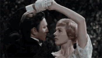 a man in a tuxedo is holding a woman 's head while they dance .