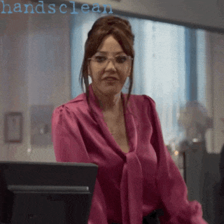 a woman in a pink blouse and glasses is standing in front of a computer screen with the words handsclean written above her