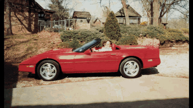 a woman is sitting in a red sports car with the top down