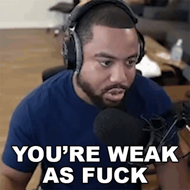 a man wearing headphones is sitting in front of a microphone and saying you 're weak as fuck