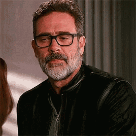 a man with a beard and glasses is wearing a leather jacket and a black jacket .