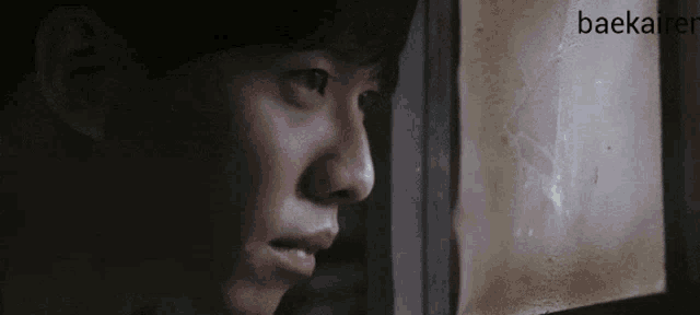 a close up of a man 's face looking out a window with the name baekaider written in the corner