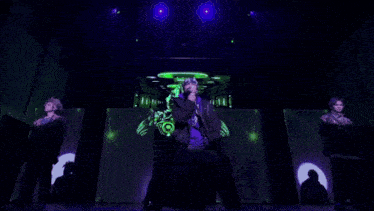 a man wearing a purple sweatshirt and a black jacket is singing into a microphone