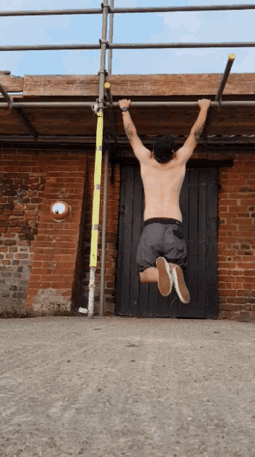 a shirtless man hangs upside down on a bar in front of a brick wall