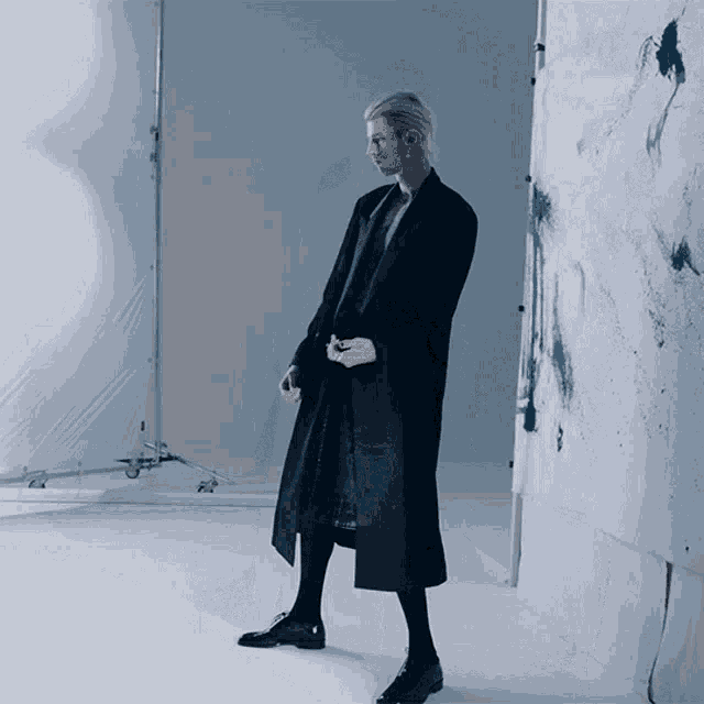 a woman in a long black coat is standing in a room