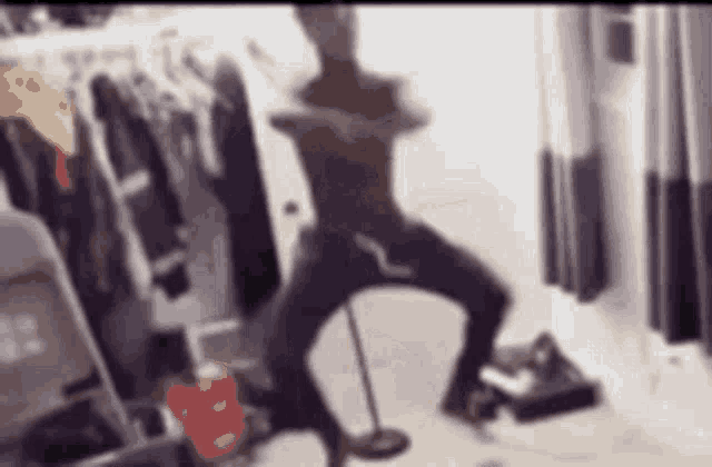 a blurry picture of a person dancing in a room with clothes hanging on the wall