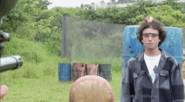 a man wearing goggles is standing in a field with barrels