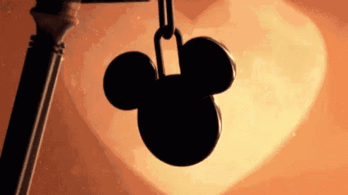 a mickey mouse key is hanging from a chain in front of a heart shaped background .