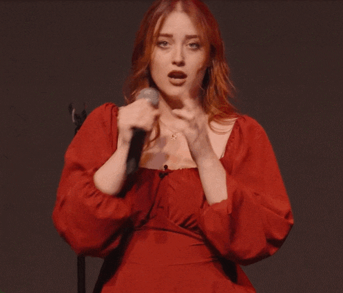 a woman in a red dress singing into a microphone with her mouth open
