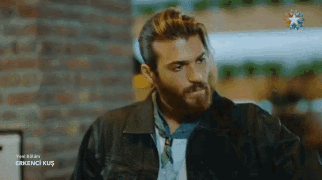 a man with a beard is wearing a black leather jacket and a blue scarf around his neck