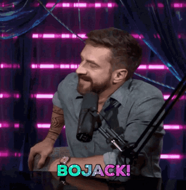 a man with a beard is sitting in front of a microphone and the word bojack is on the screen behind him
