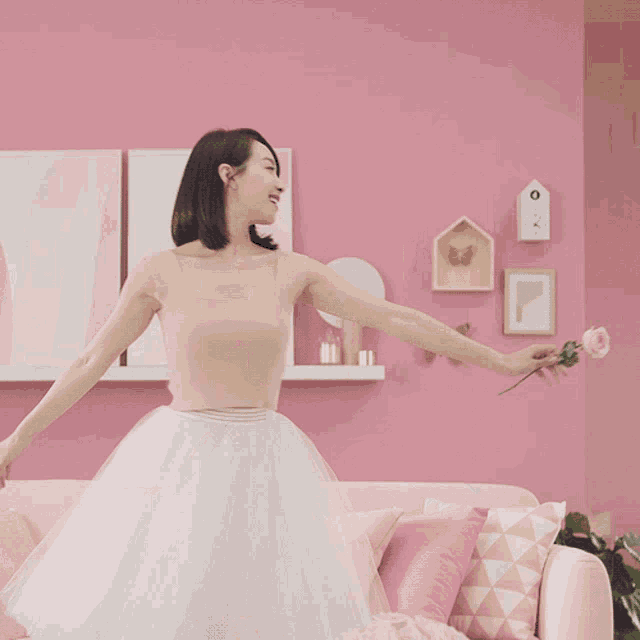 a woman in a white skirt is dancing in front of pink walls