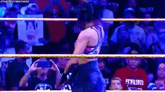 a woman is standing in a wrestling ring with a crowd watching and taking pictures .