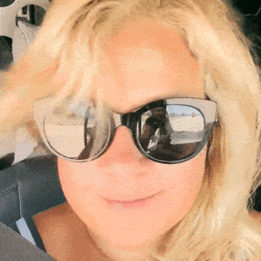 a woman wearing sunglasses takes a picture of herself in the mirror