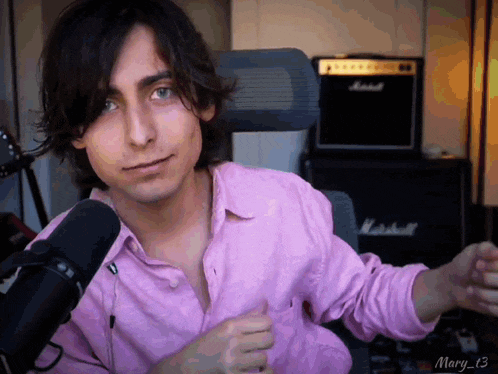 a man in a pink shirt is sitting in front of a marshall amp