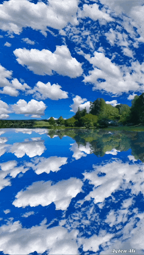 a blue sky with white clouds and trees reflected in a lake