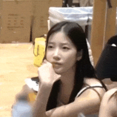 a woman with long black hair is sitting on a wooden floor with her hand on her chin