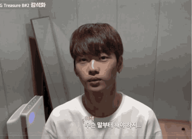 a young man in a white shirt stands in front of a wall with g treasure b # 2 written on it