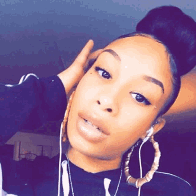 a woman wearing hoop earrings and a bun is taking a selfie