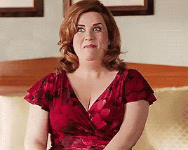 a woman in a red floral dress is sitting on a couch and making a funny face .