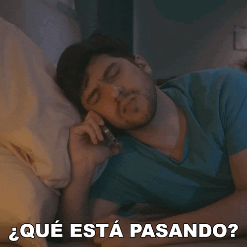 a man laying in bed talking on a cell phone with the words " que esta pasando " written below him