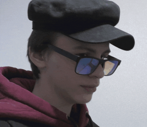 a young man wearing sunglasses and a hat looks to the side