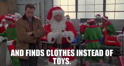 a man in a suit is standing next to santa claus in a room with elves .