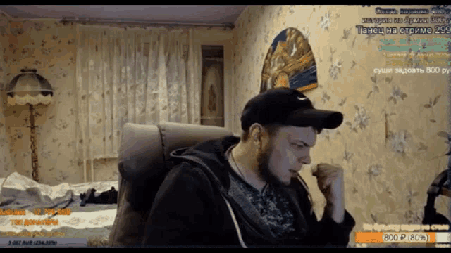 a man in a hat is sitting in a chair in front of a screen that says ' twitch ' on it