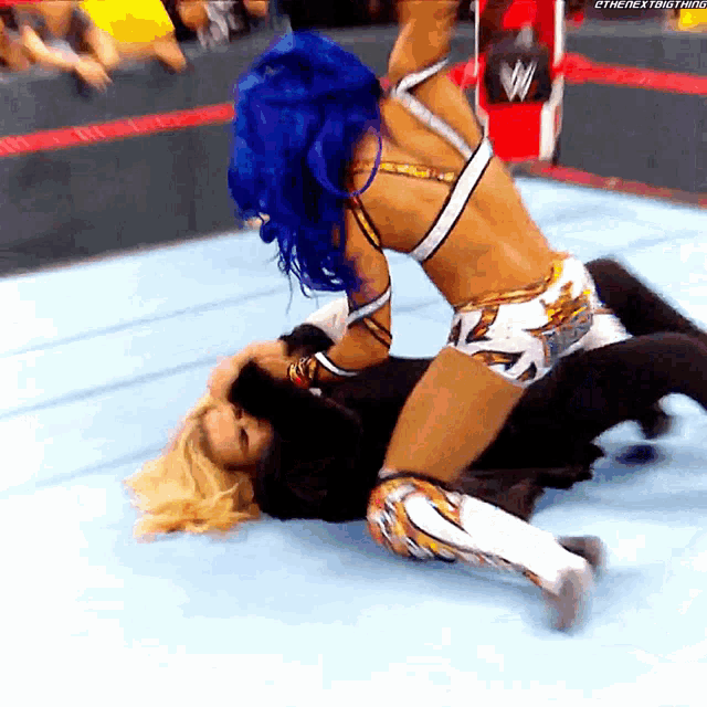 a female wrestler with blue hair is wrestling another wrestler