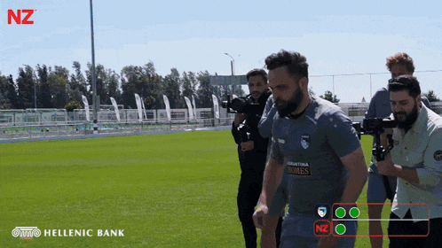 a man in a hellenic bank shirt is being filmed