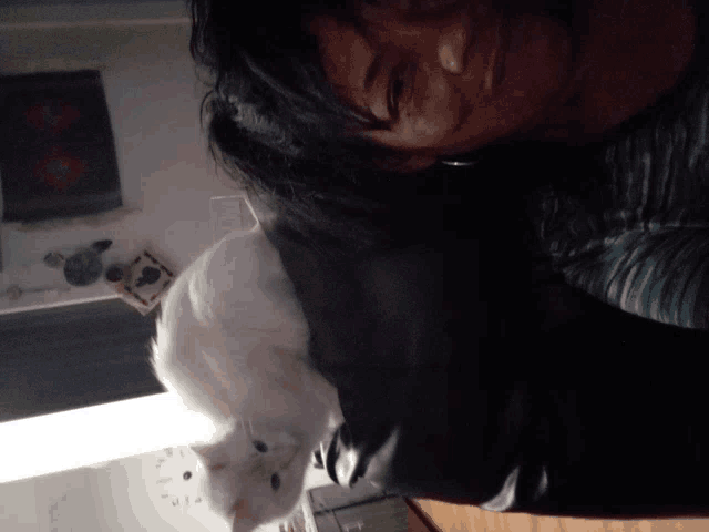 a woman laying on a bed with a white cat on her shoulder
