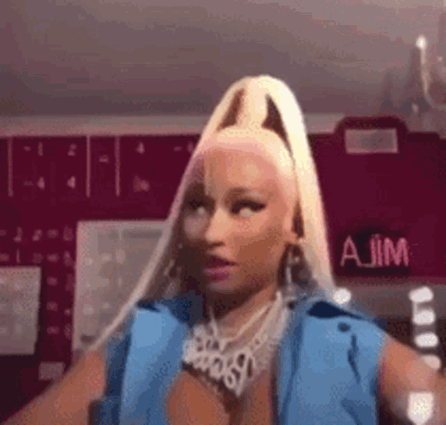 a woman with blonde hair and a blue vest is standing in front of a pink wall .