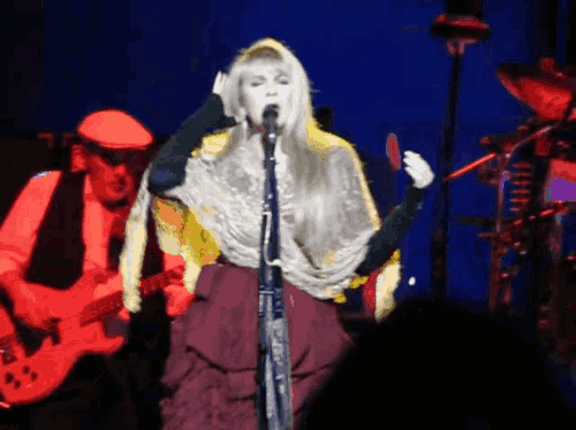 a woman singing into a microphone while a man plays a guitar in the background