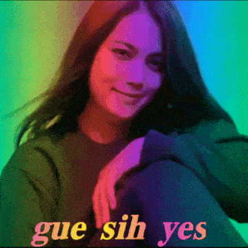 a woman is sitting in front of a rainbow background with the words gue sih yes