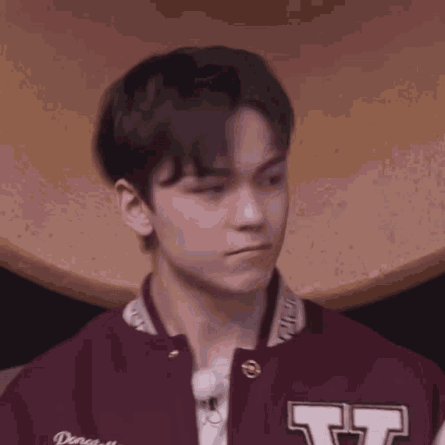 a close up of a young man wearing a maroon varsity jacket and a white shirt .