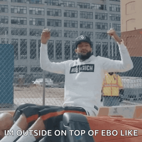 a man is sitting in a car with his arms in the air and the caption im outside on top of ebo like .