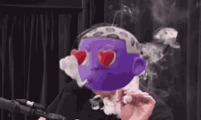 a man is smoking a cigarette in front of a microphone with a purple mask with heart shaped eyes .
