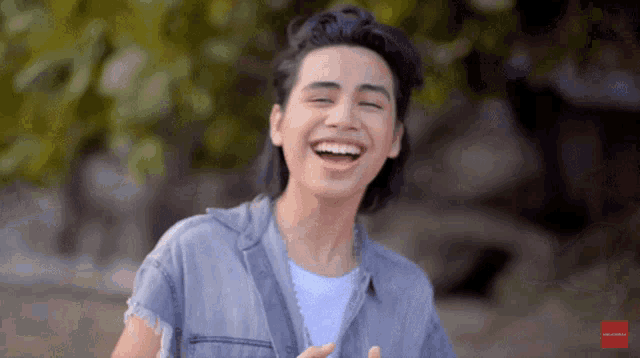 a man in a denim shirt is laughing in front of a blurred background with a red arrow pointing to the bottom