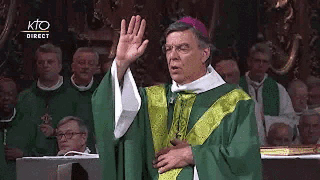 a priest in a green and yellow robe is giving a speech in front of a crowd .